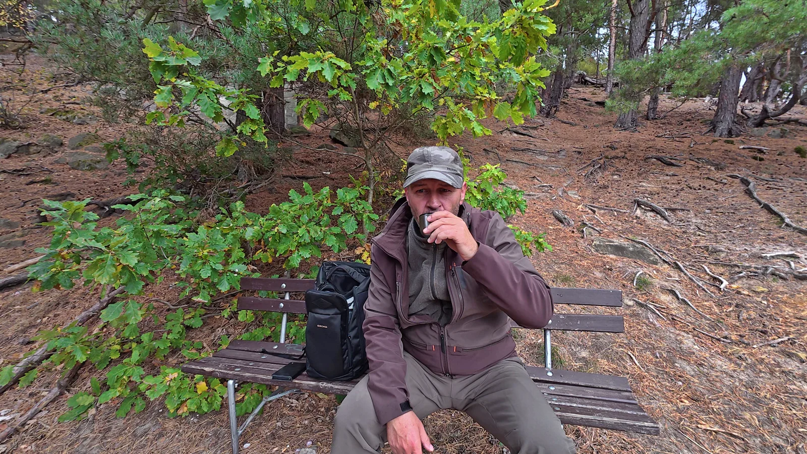 Marco macht mit einem Becher eine Pause auf einer Bank im Wald